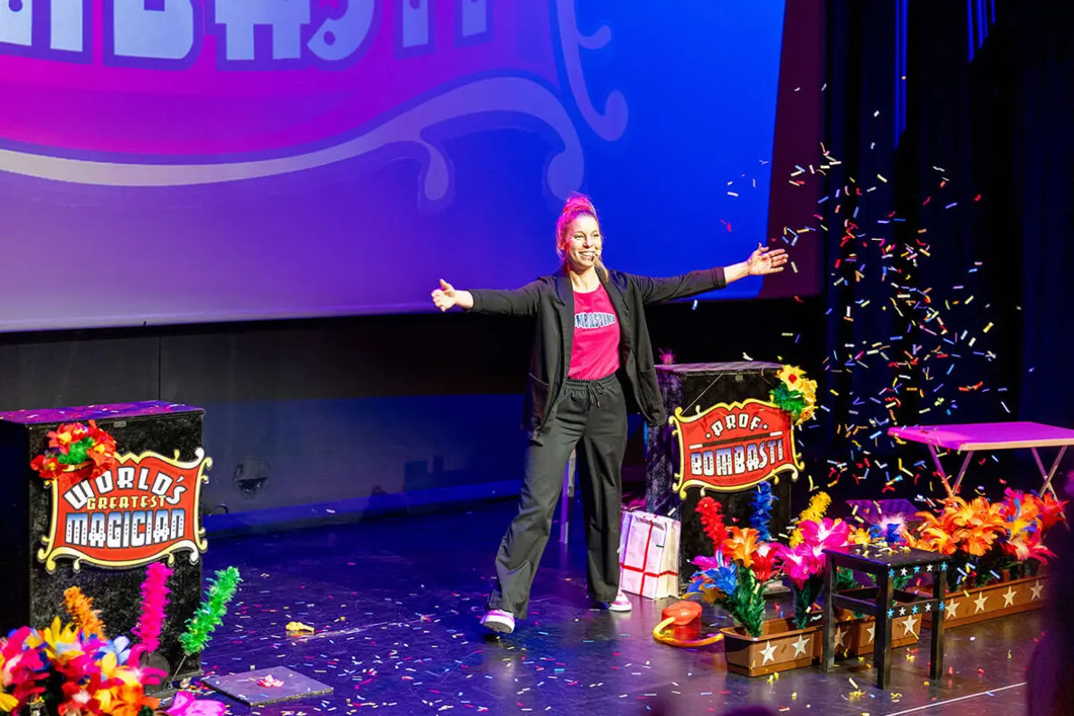 Kinderzauberin Bombastini steht strahlend auf der Bühne mit ausgebreiteten Armen im bunten Konfettiregen beim Show-Finale